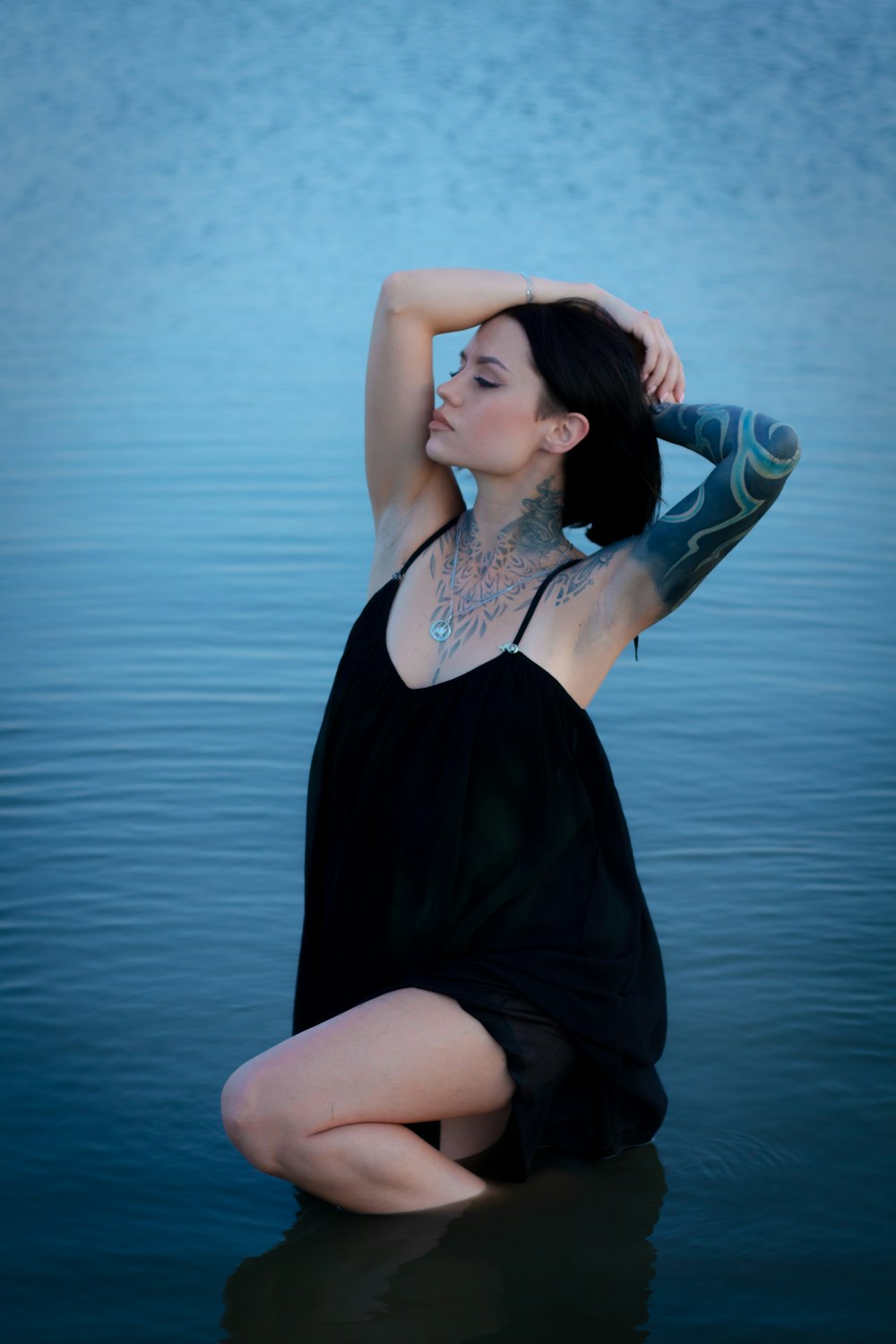 woman in black dress sitting on blue body of water during daytime