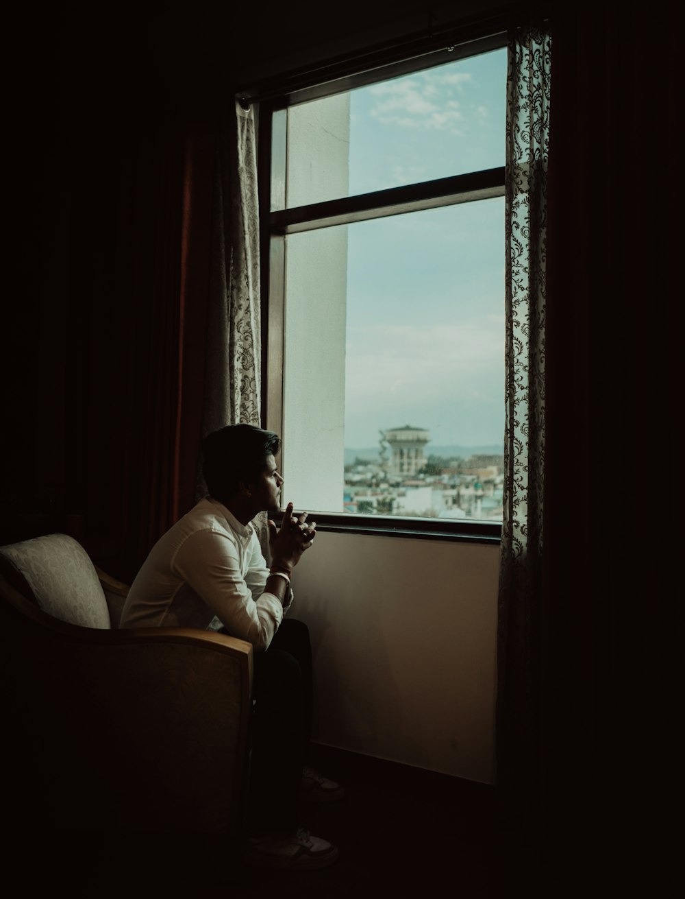 man in white dress shirt sitting on chair near window during daytime