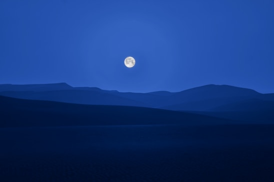 A serene night sky with a full moon illuminating a calm landscape.