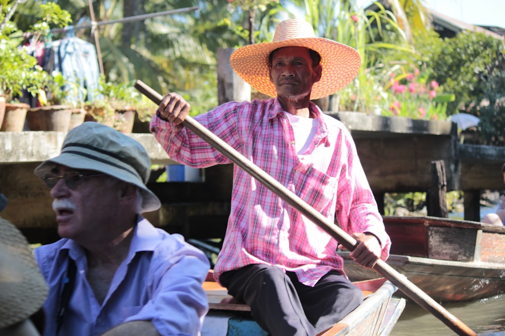 man in pink dress shirt and brown hat sitting on brown wooden bench during daytime