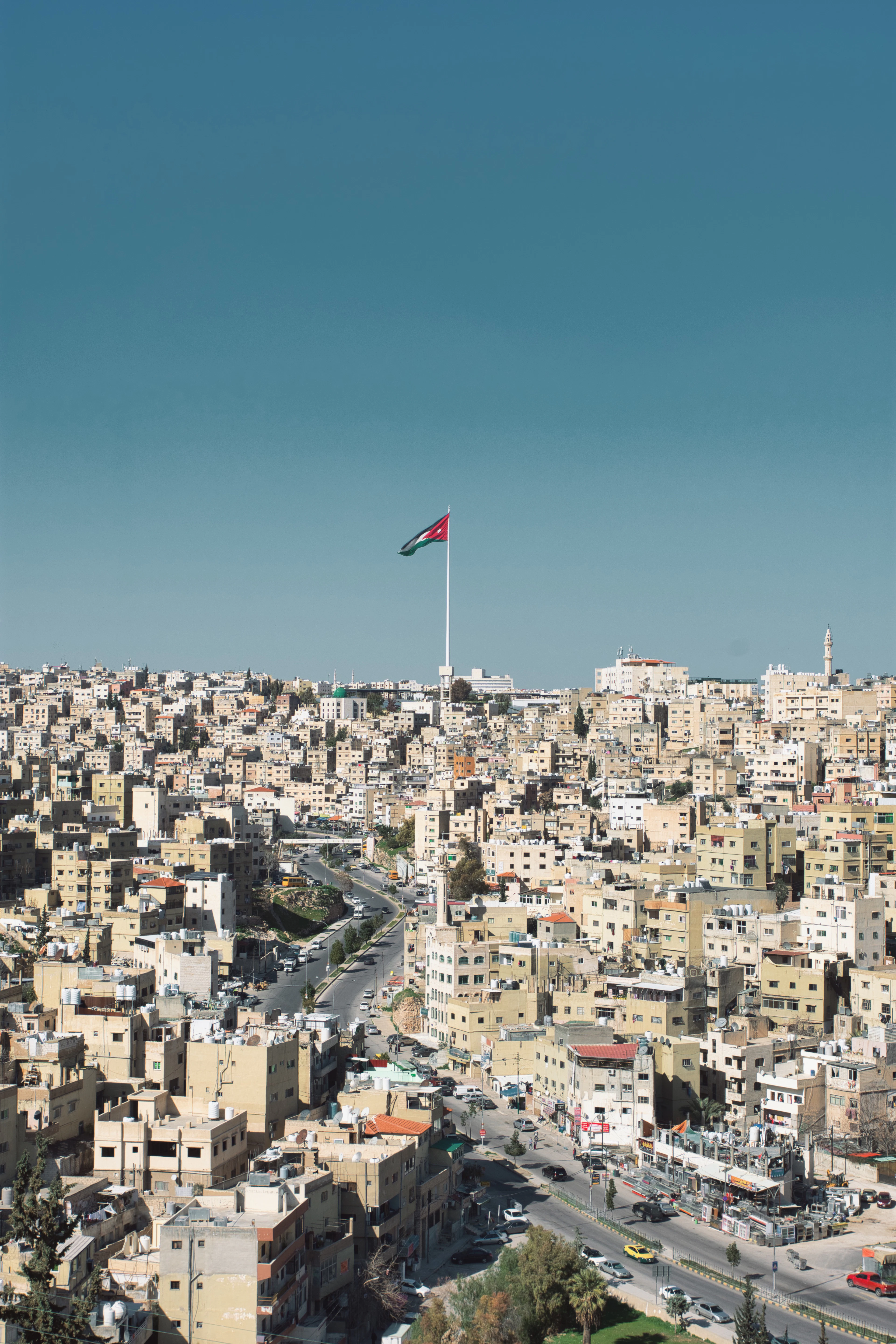 The hills of Amman covered in sand-colored buildings, with the giant Jordanian flag flying above the city on its towering flagpole