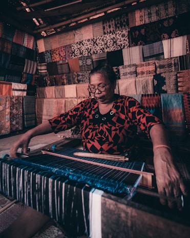 A joyful woman artisan weaving fabric in a sunlit workshop surrounded by natural materials.