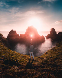 woman in white shirt standing on cliff during sunset