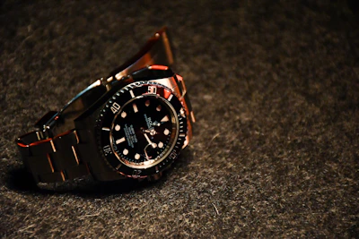 A luxury watch with a gold bezel and black leather strap displayed on a polished surface.