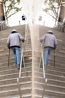 A technician carefully installing an easystep device on a wooden staircase with an elderly man watching