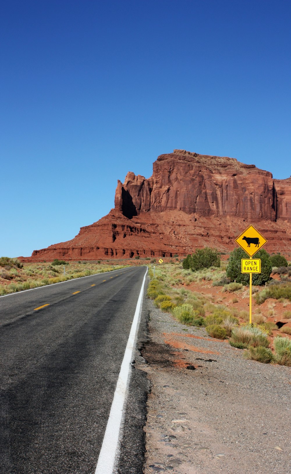 yellow and black road sign near brown rock mountain under blue sky during daytime