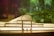 A detailed miniature model of an architectural structure with an arched glass roof and multiple windows is illuminated from within. The background features a soft, blurry display of green and purple hues that create a dreamy, atmospheric effect.