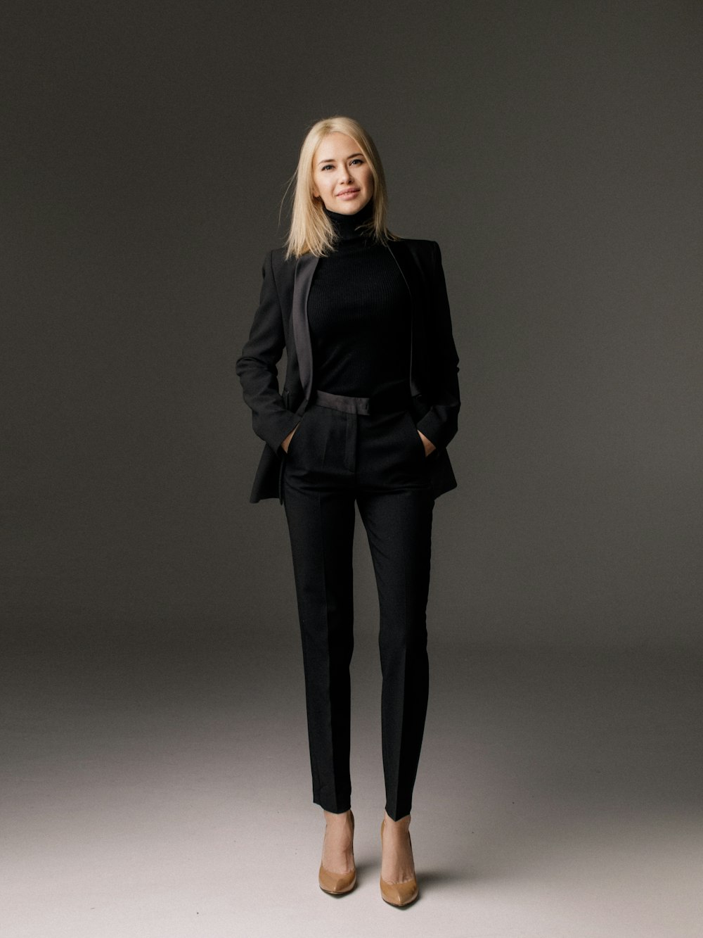 Model in precise black tailoring photographed against a neutral studio backdrop