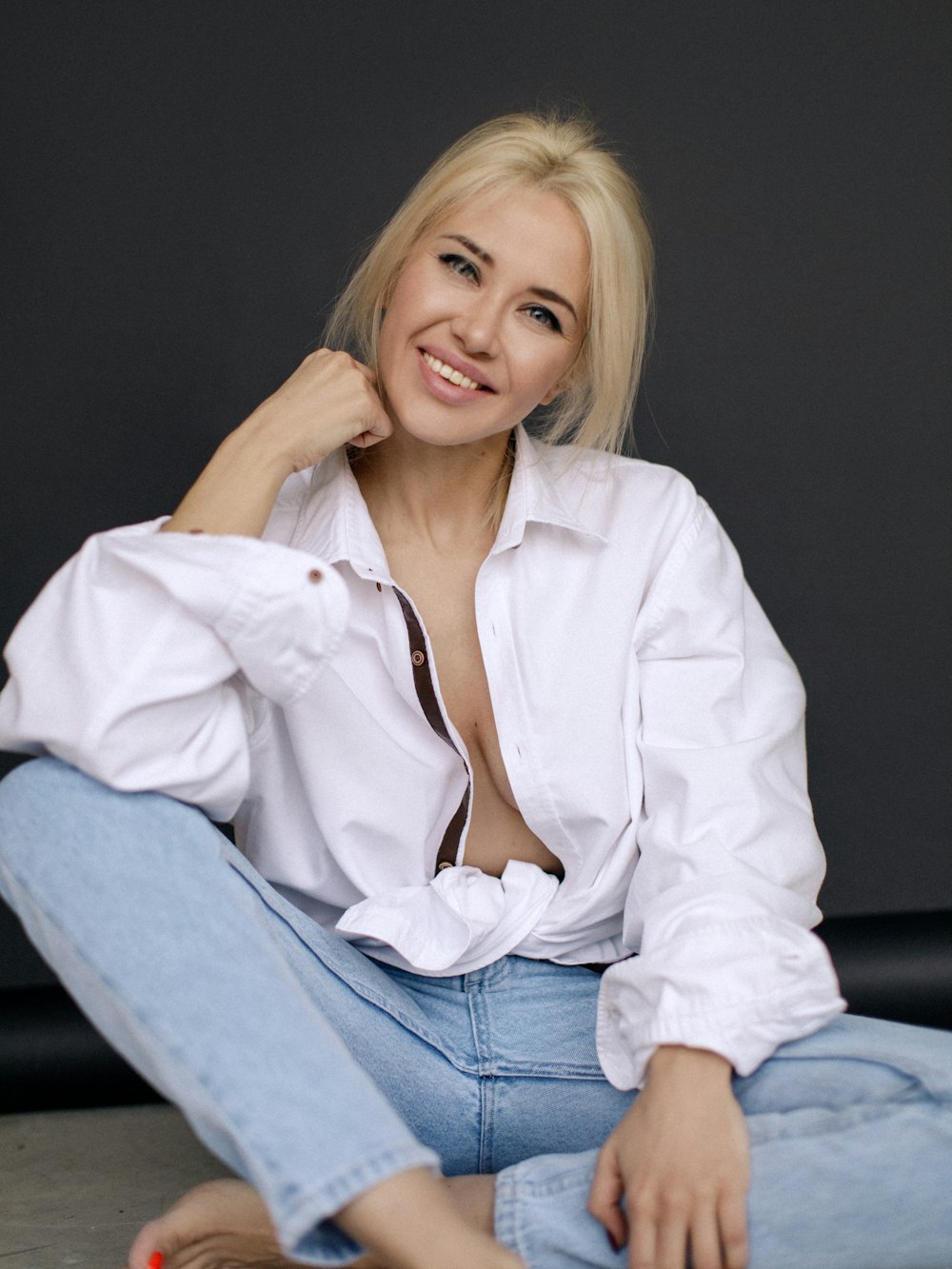 woman in white dress shirt and blue denim jeans sitting on black leather couch