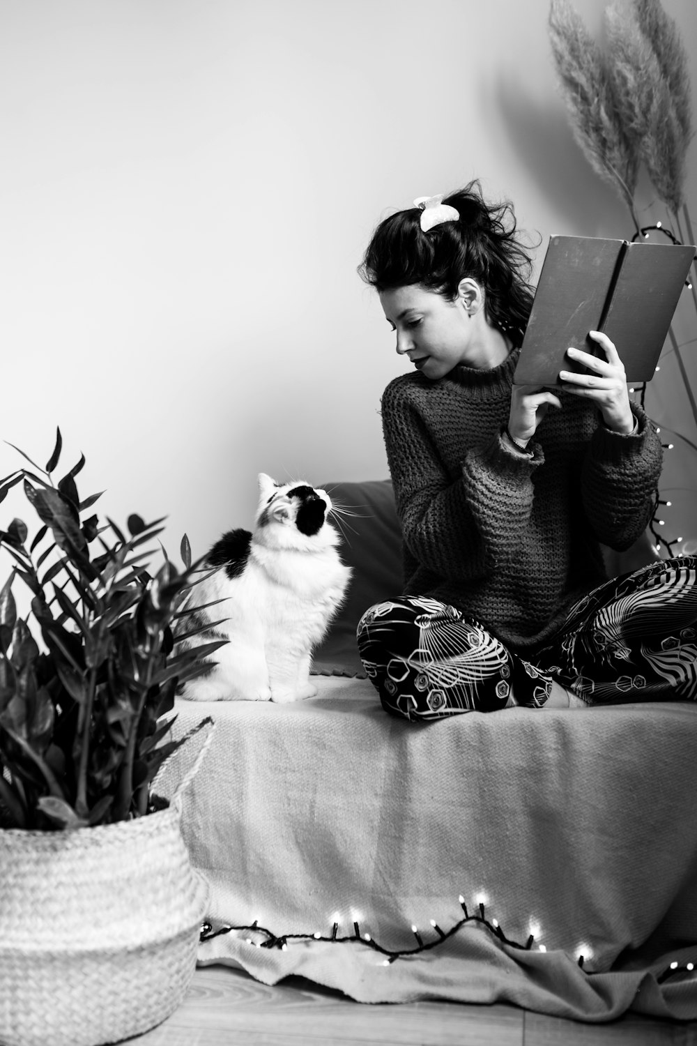 grayscale photo of woman sitting on bed using laptop