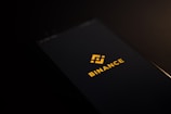 A smartphone screen displaying the Binance logo with yellow text and an icon in the center against a dark background.