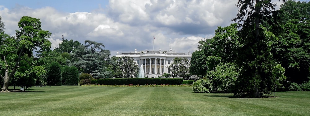 white concrete building near green grass field under white clouds during daytime