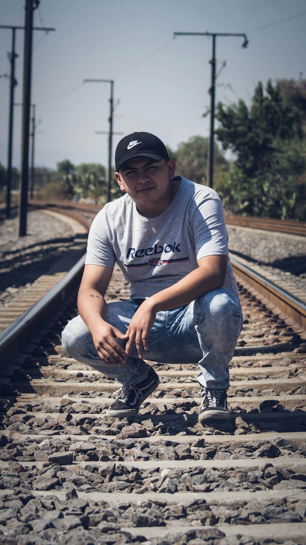 man in white crew neck t-shirt and blue denim jeans sitting on train rail during