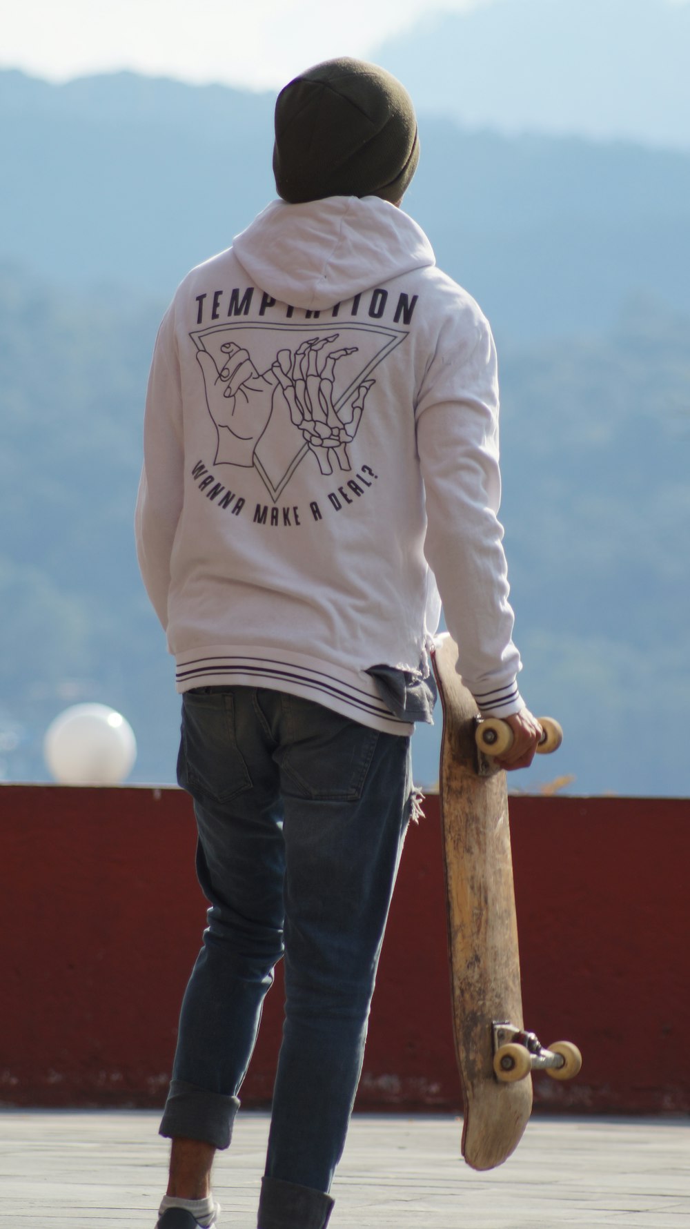 man in white and black sweater and blue denim jeans standing on brown wooden fence during