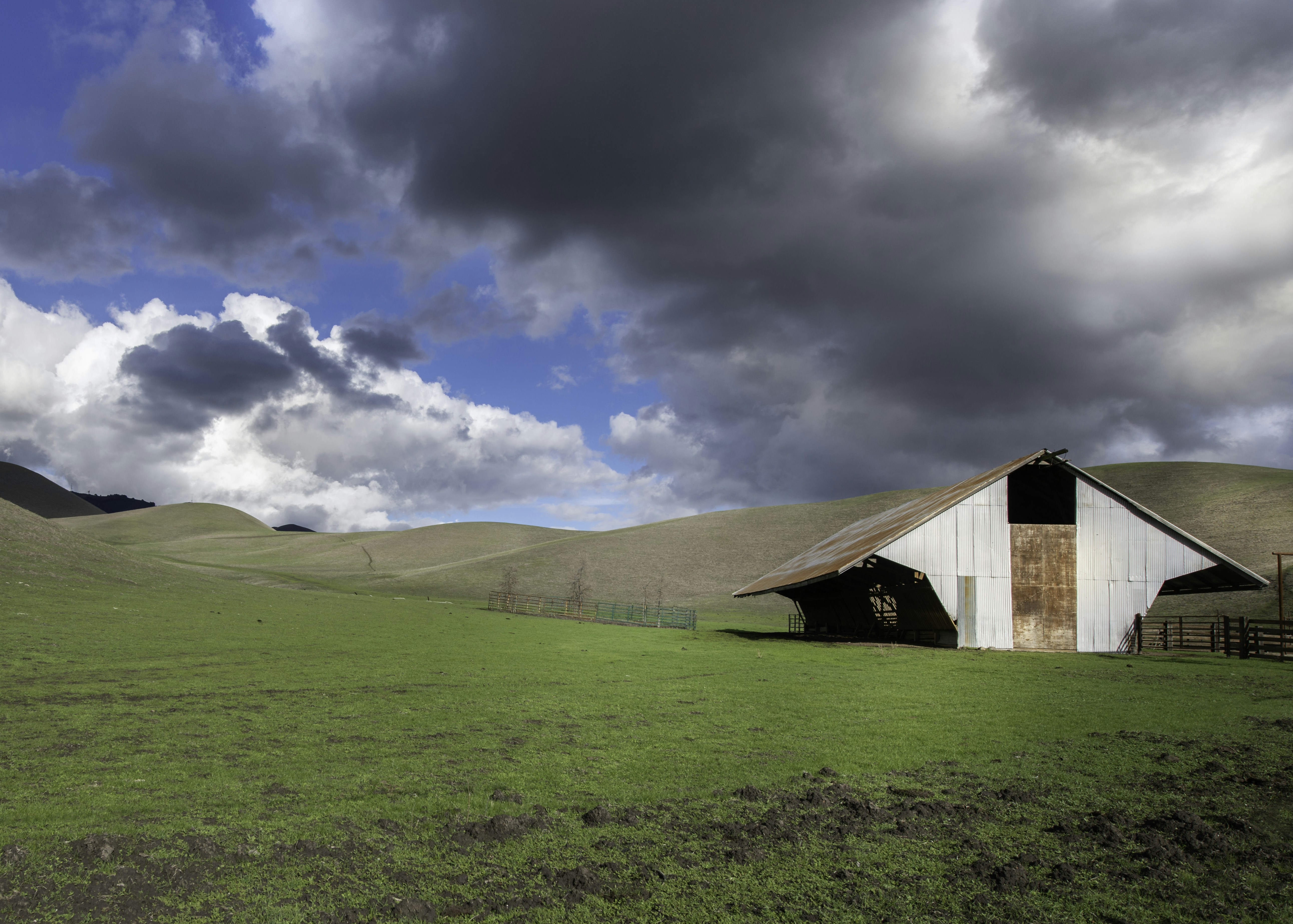brown wooden barn on green grass field under blue sky and white clouds during daytime, A blending of dark and white clouds make for a mysterious, ominous landscape.