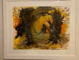 A framed abstract painting features a vivid display of colors and shapes, with a predominant use of dark and earthy tones. Silhouetted tree forms and branches create a mysterious, woodland scene. The background displays a blend of oranges and yellows, evoking a sense of warmth and depth.