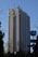 A tall hotel building with numerous windows and a logo labeled 'Hotel Marinela' near the top. In the foreground, there are bare trees and a sign with a subway symbol and street name written in both Cyrillic and English. The sky is clear and blue, suggesting it is daytime.
