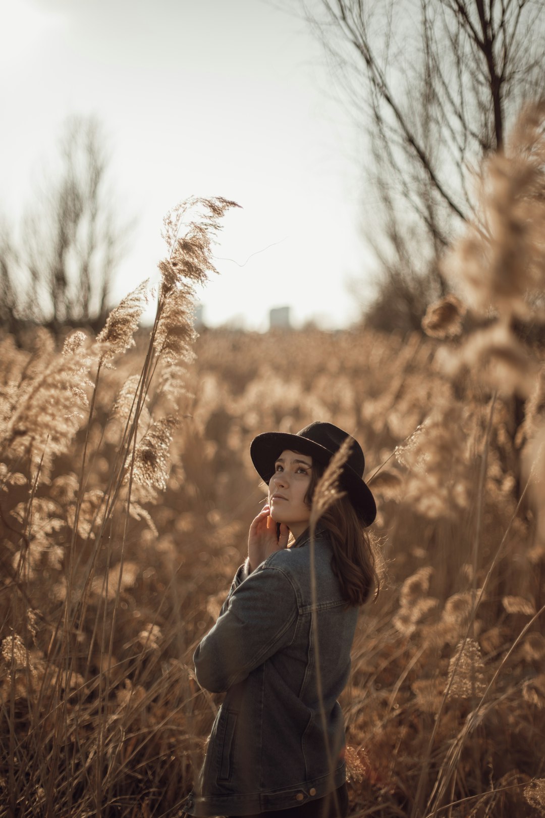 woman in grey jacket wearing black hat standing near brown grass during daytime