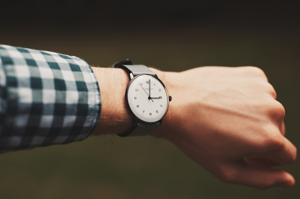 person wearing silver round analog watch with black leather strap