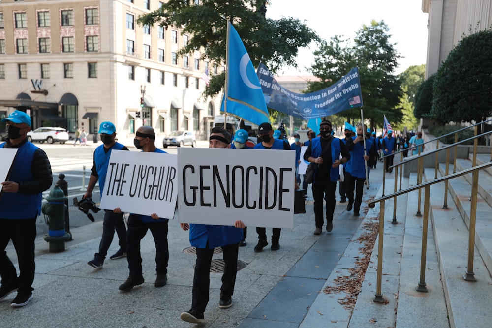 people standing on sidewalk holding blue and white banner