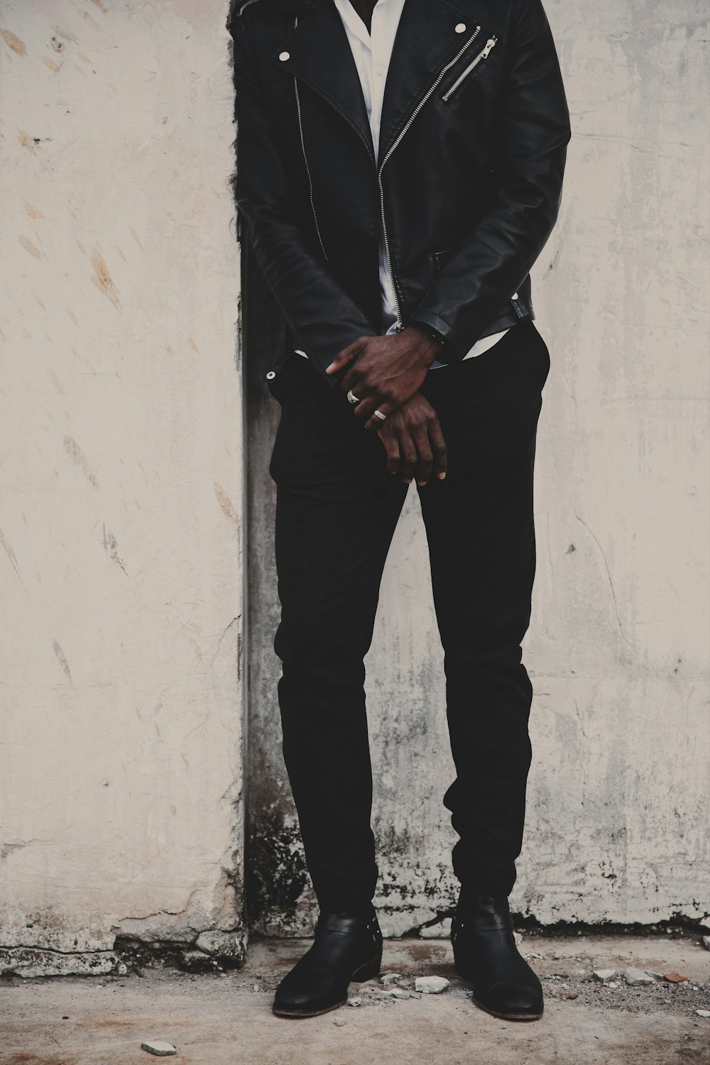 man in black jacket and black pants standing beside white wall