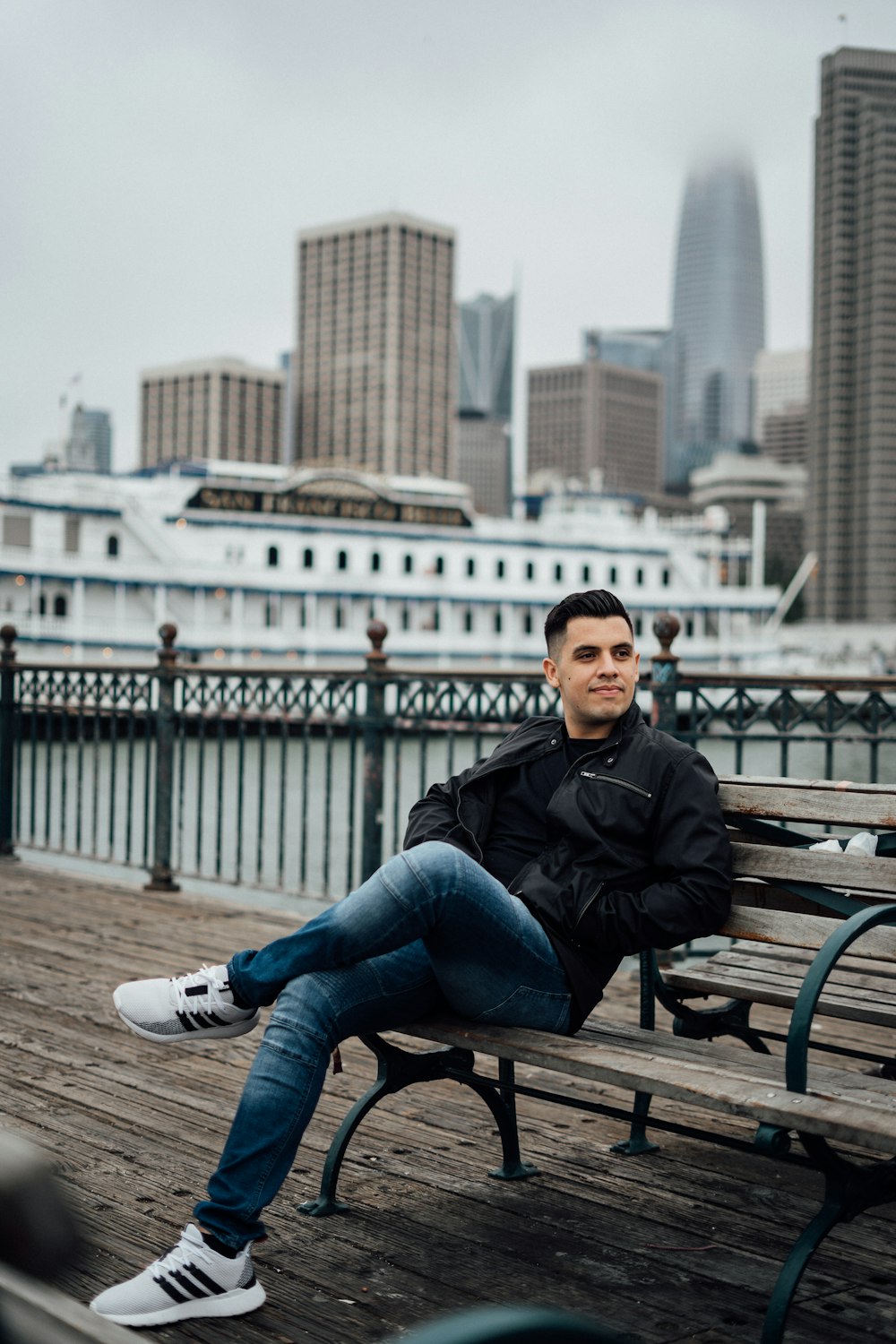 man in black jacket and blue denim jeans sitting on brown wooden bench during daytime