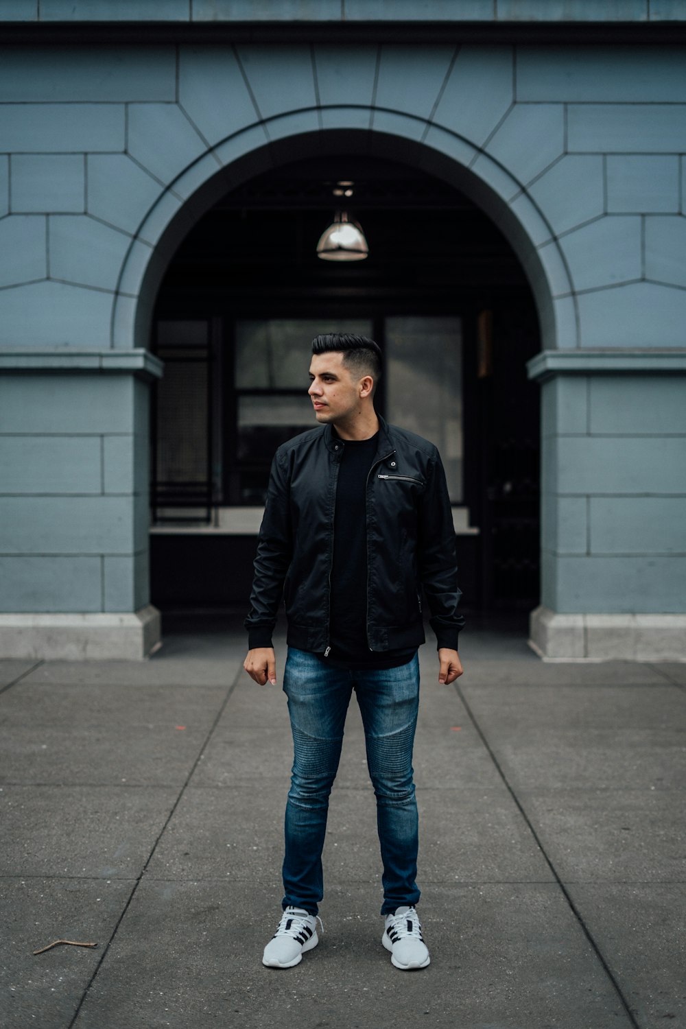 man in black zip up jacket standing near black metal gate during daytime