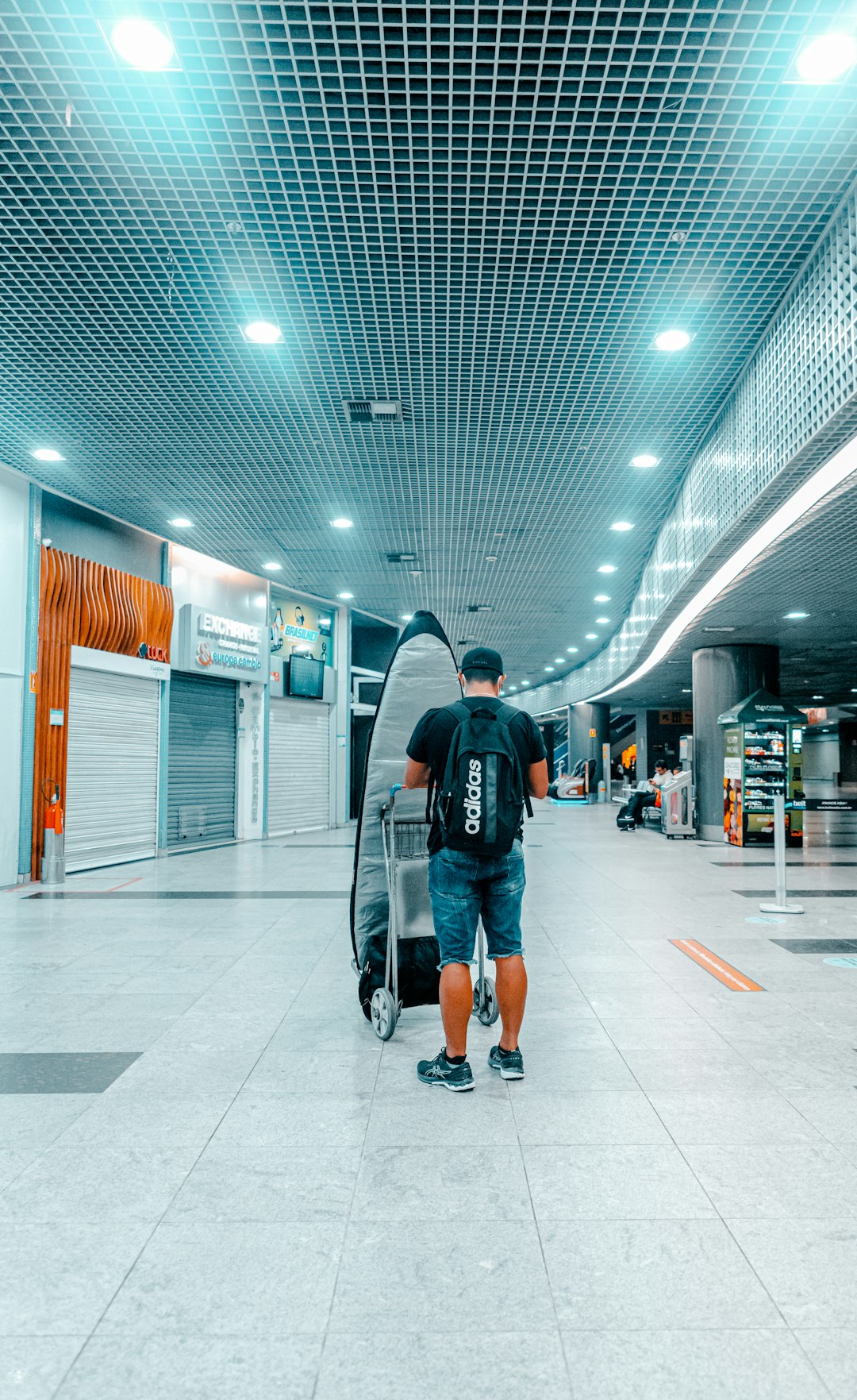 man in black jacket and blue denim jeans walking on white floor tiles