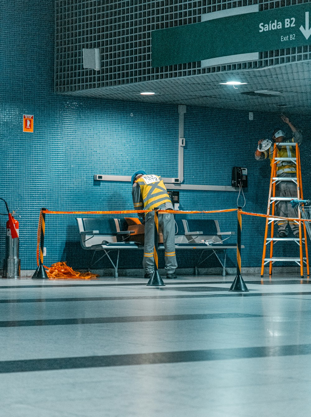 man in yellow and black jacket and black pants standing near gray metal table