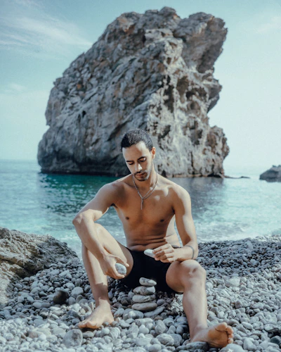 topless man sitting on rock near body of water during daytime