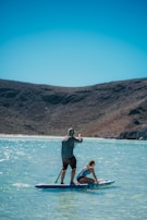 man in black shorts and blue shirt sitting on brown wooden boat on blue sea during