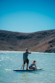 man in black shorts and blue shirt sitting on brown wooden boat on blue sea during