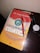 A book titled 'La Curación Cuántica' by Dr. Frank Kinslow is lying on a dark wooden surface. On top of the book is a red pen and next to it is a wristwatch with a black leather strap.