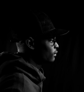 Side profile of a model sporting a bold black cap and matching jacket in natural light.