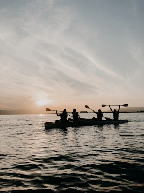 A group of friends paddling kayaks on calm blue waters at sunset.
