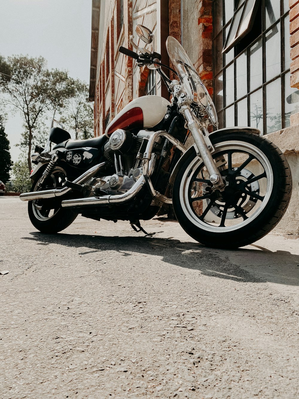 red and black cruiser motorcycle parked beside brown wooden house during daytime