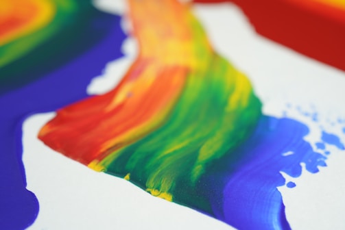 A vivid, flowing spectrum of colors that blend seamlessly together, including red, orange, yellow, green, blue, and purple, appearing as broad, sweeping brushstrokes. The colorful stripes create a dynamic and energetic visual effect.