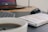 A desk setup with a laptop, mechanical keyboard, mouse, book titled 'Habitos Atomicos', and a cup of coffee. The background is a soft focus, highlighting the foreground items on a wooden table with a black mat.