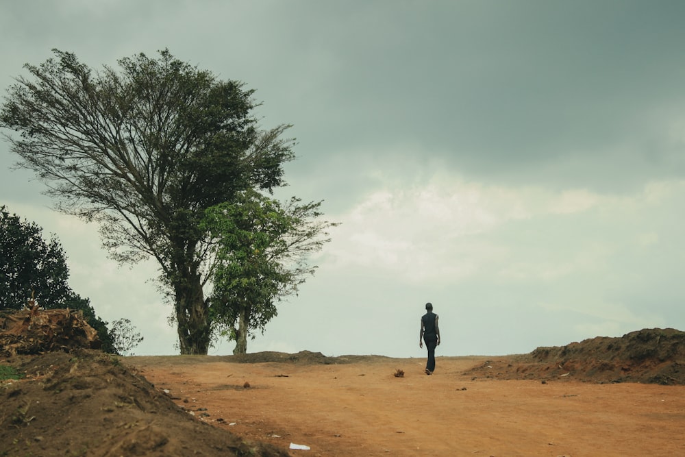 man in black jacket walking on brown sand near green tree during daytime