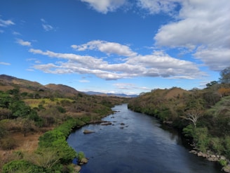A serene river flowing through a lush green valley under a calm sky.