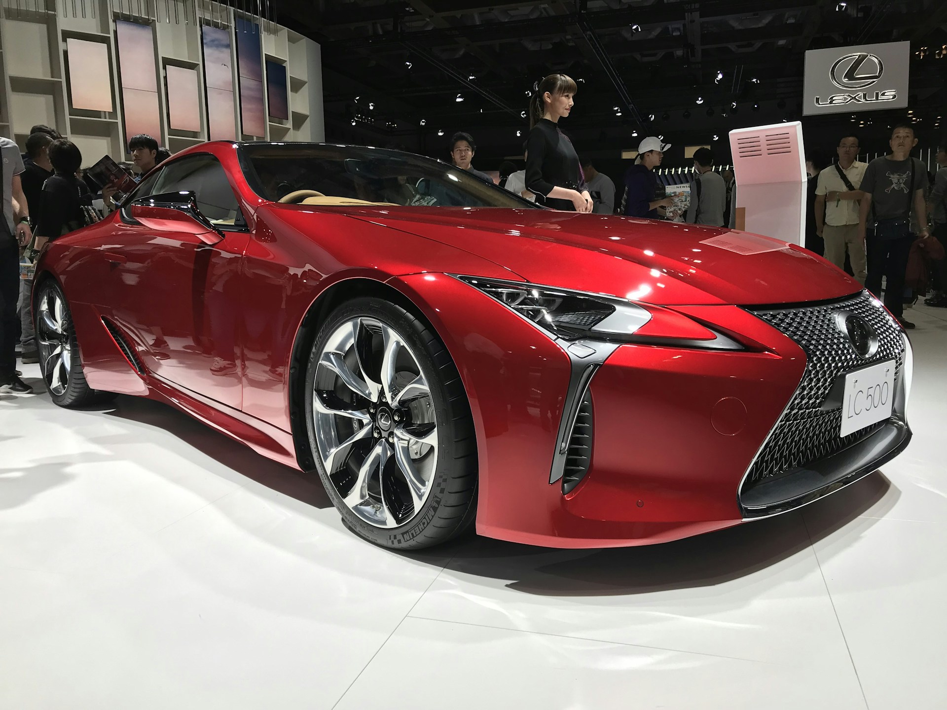 A sleek red sedan gleaming under the showroom lights, showcasing its polished curves and shiny alloy wheels.