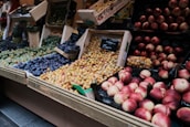 A market stall displaying a variety of fresh fruits arranged in wooden crates and baskets. There are different types of plums, peaches, and grapes, showcasing various colors ranging from purple to red to yellow. The setup is visually appealing with ripe fruits in abundance and a rustic market atmosphere.