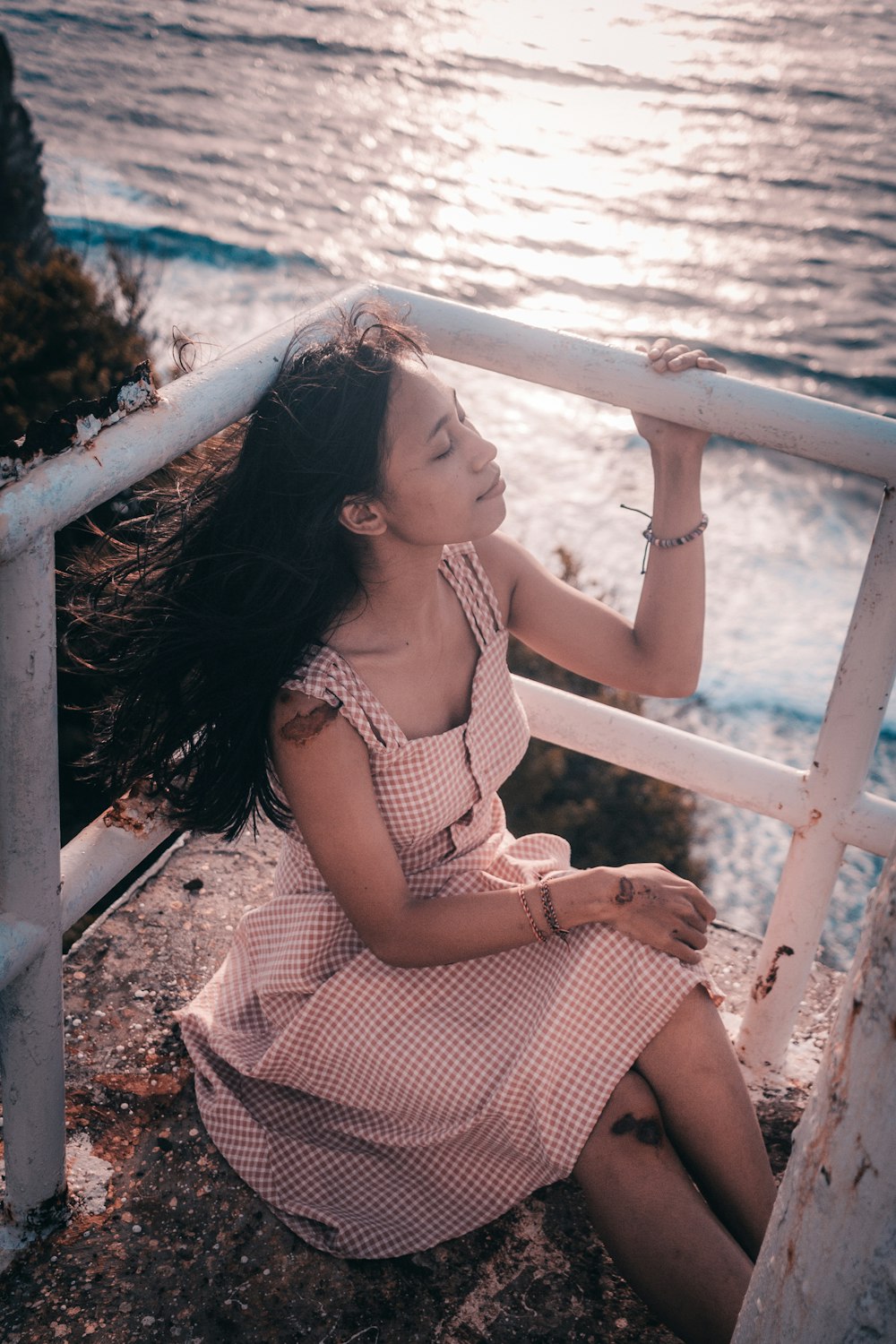 woman in white and brown plaid dress sitting on white wooden fence during daytime