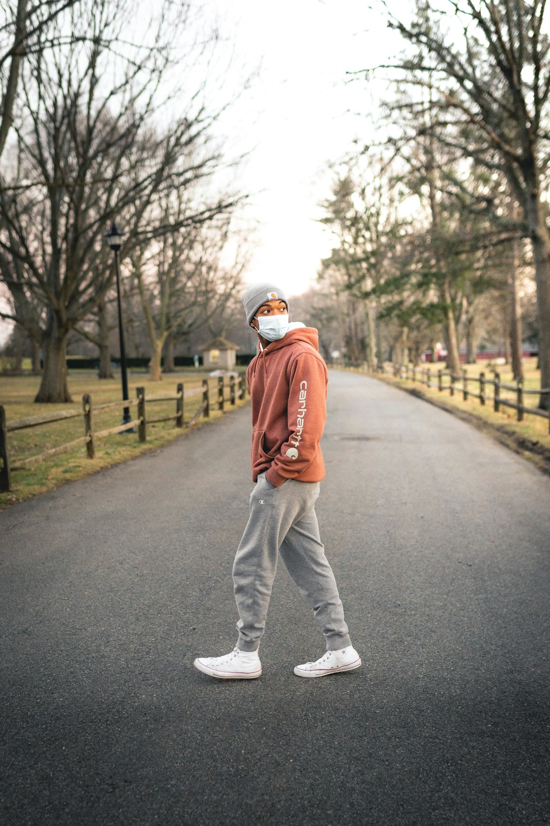 man in orange jacket and white pants walking on gray asphalt road during daytime