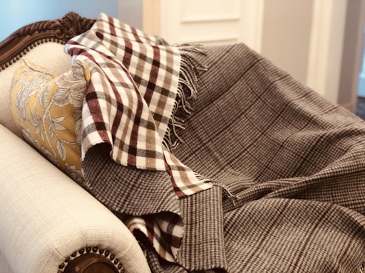 A plush, ornately carved sofa is draped with a patterned, brown and white checked blanket. A soft, floral-patterned pillow in gold hues complements the luxury of the setting.