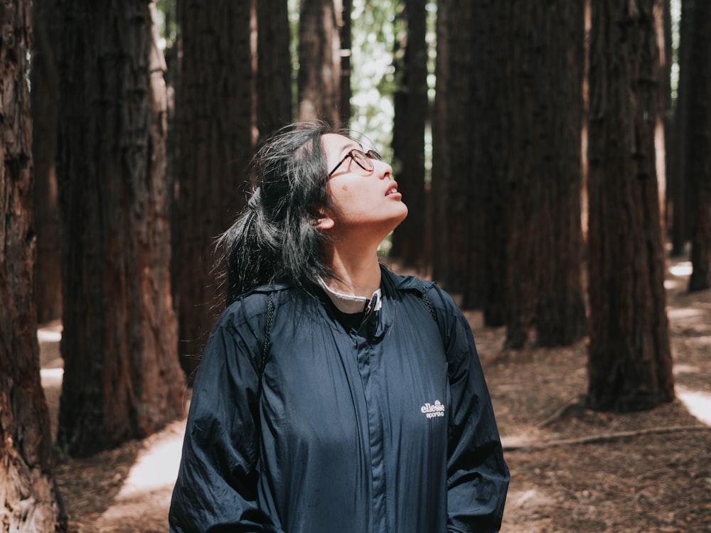 femme en veste noire debout près des arbres pendant la journée