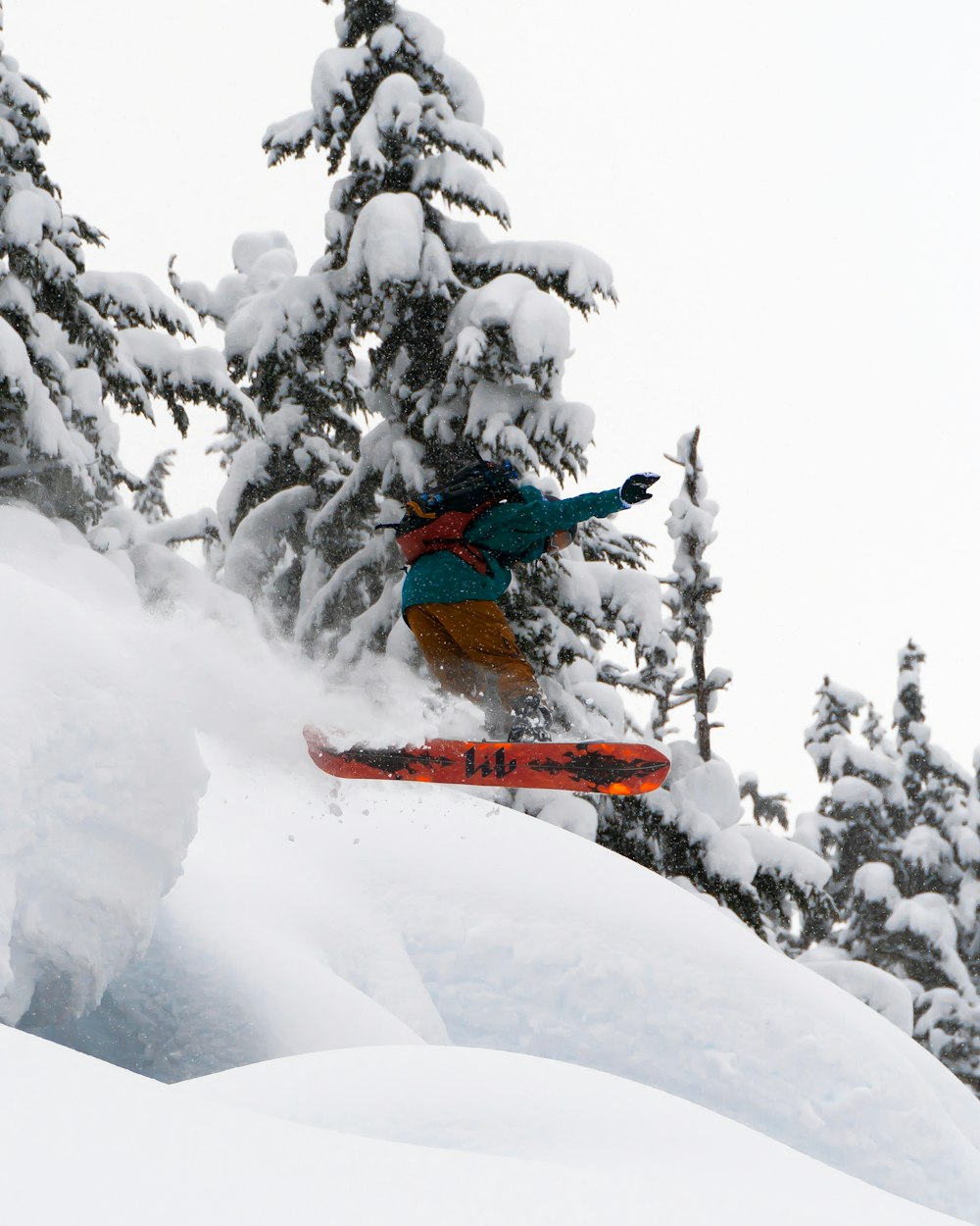 hombre en chaqueta azul y pantalones naranjas montando una tabla de esquí naranja en un terreno cubierto de nieve durante