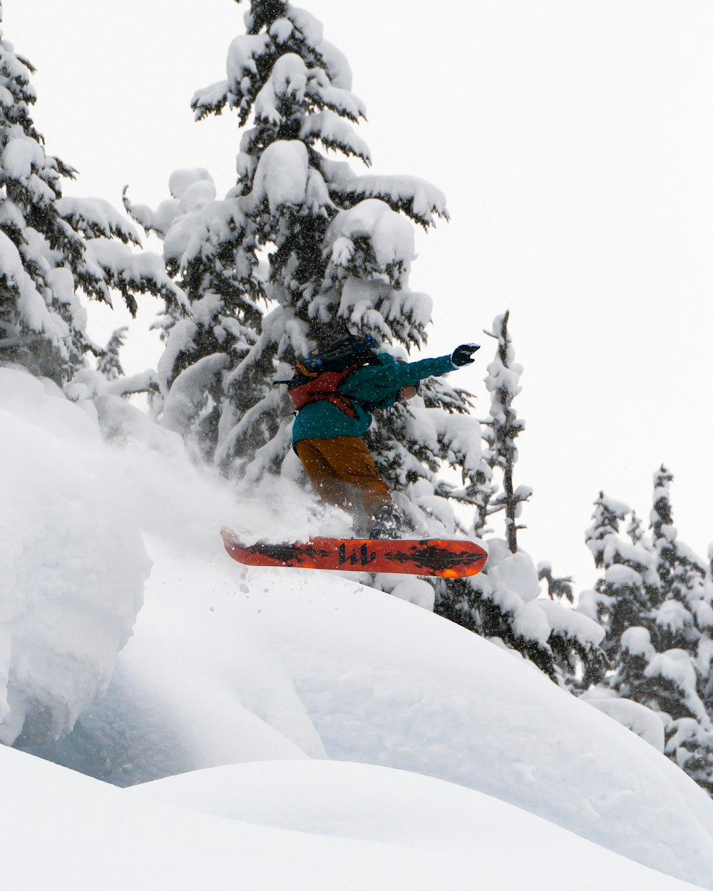 man in blue jacket and orange pants riding orange ski board on snow covered ground during