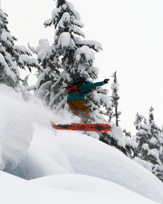 A snowboarder airing off a snow pillow between heavily snow-laden trees at Revelstoke
