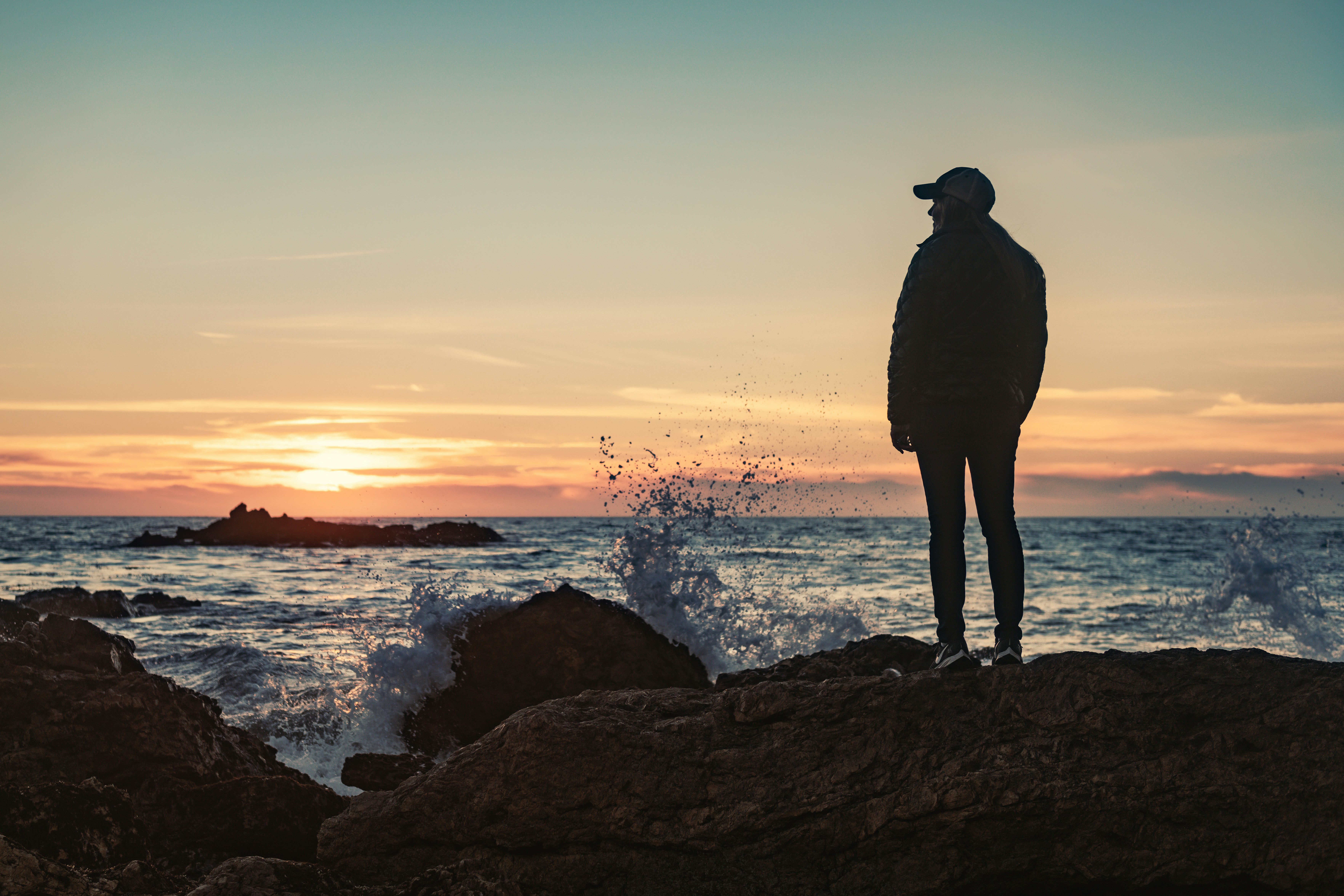 silhouette of man standing on rock formation near body of water during sunset